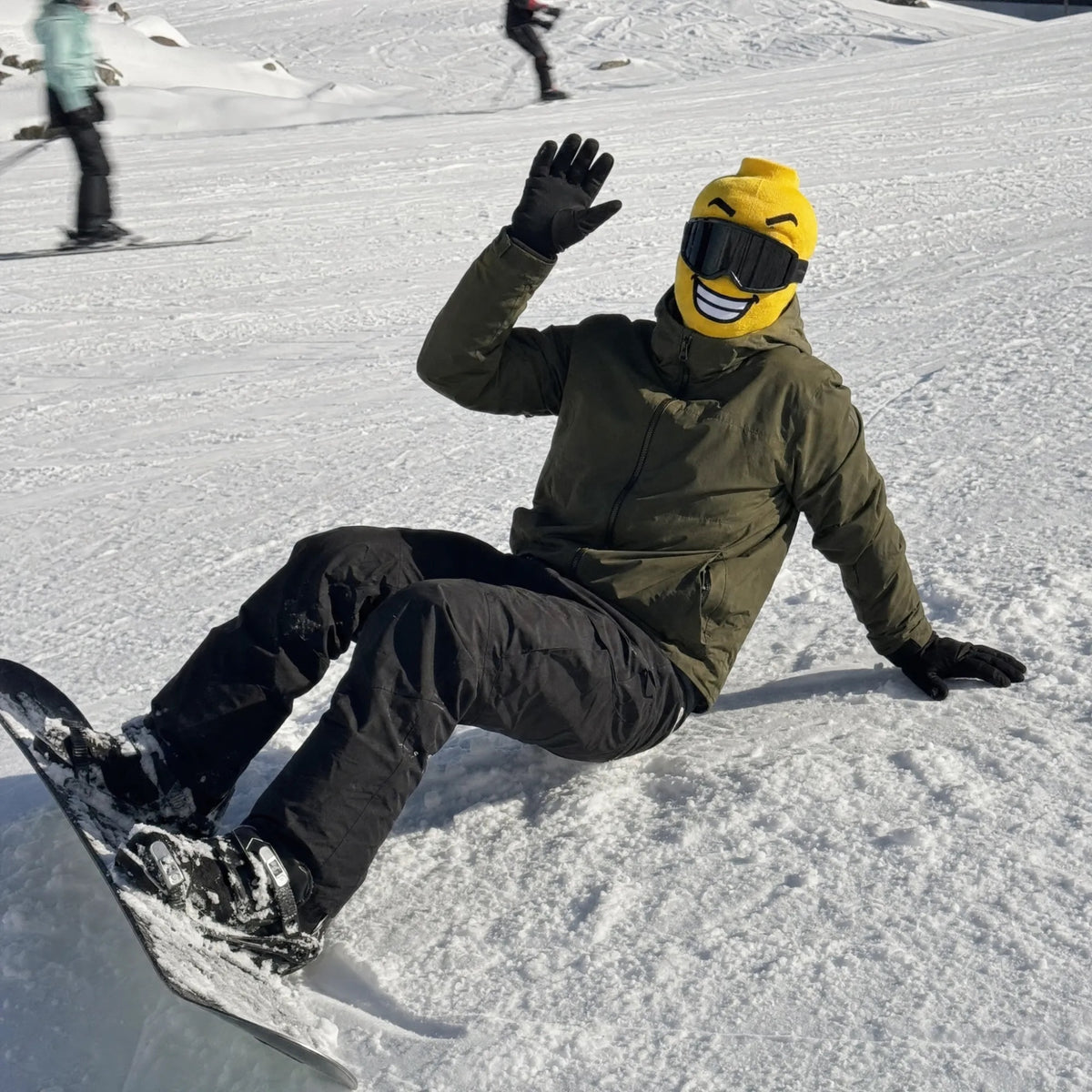 Snowboarder in a Balakoo Sunny mask waving from the snow