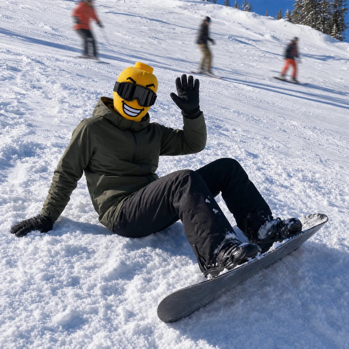 Snowboarder sitting on the slope waving, wearing a Balakoo ski mask
